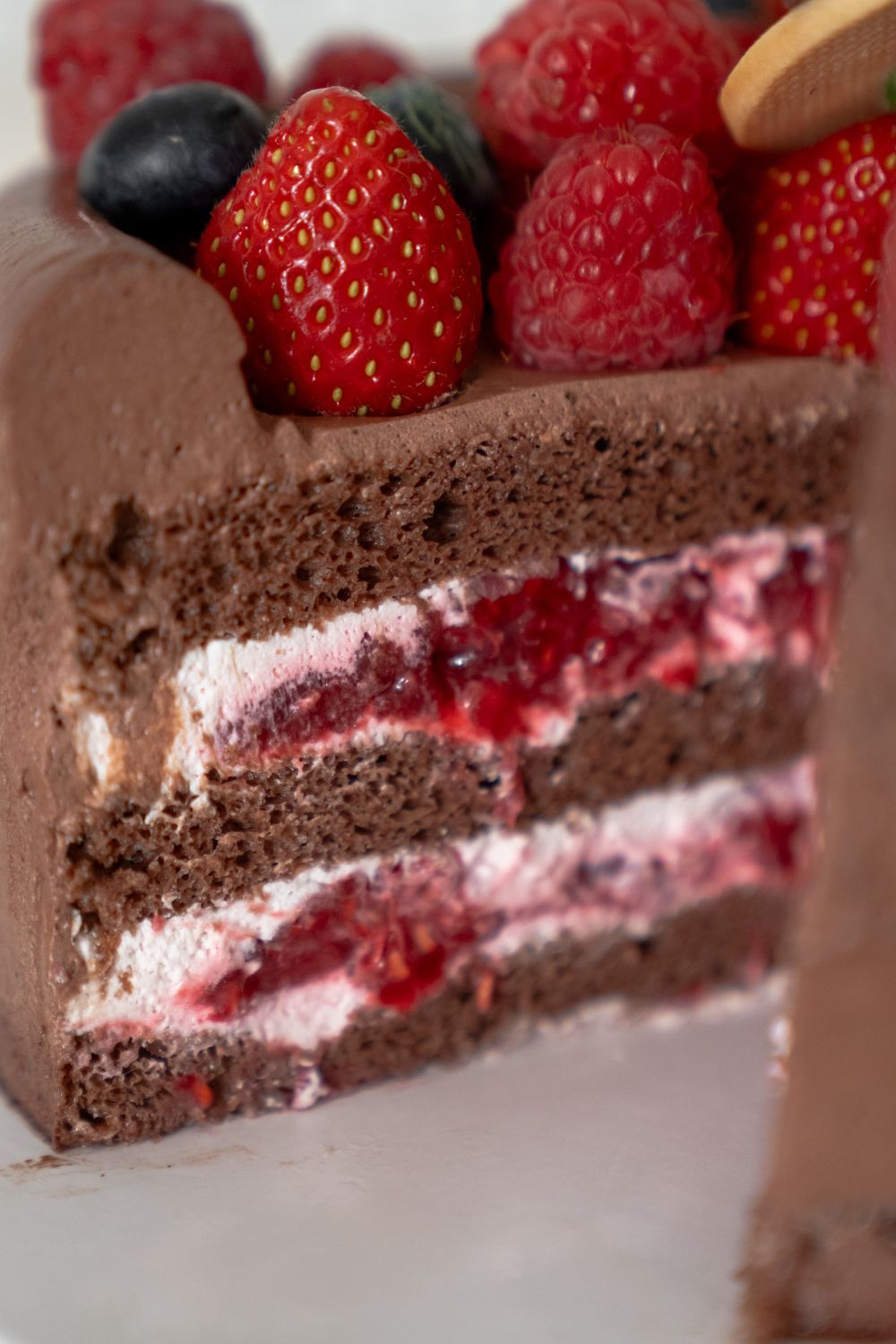 Close-up of a chocolate cake with raspberry cream layers and berries on top